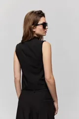 Chaleco sastrero negro de escote en V, con cierre frontal de botones y bolsillos ribeteados simulados. Presenta terminación en punta en el delantero y diseño entallado de inspiración tailoring.