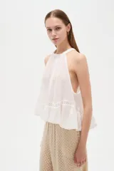 Top blanco de algodón con cuello halter, diseño holgado y detalle de encaje en el borde inferior.