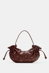 Bolso de hombro de diseño fruncido con cordones ajustables en los laterales y tachas metálicas doradas distribuidas por toda la superficie. Cuenta con asa corta de hombro y cierre superior con cremallera.