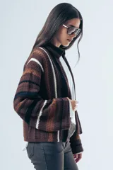 Cardigan de tejido de punto con diseño a rayas horizontales en tonos marrones, negros y blancos. Presenta un corte relajado, cuello alto y mangas largas amplias.