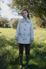 Chaqueta rosada de corte holgado con detalles en estampado de cuadros escoceses en el cuello, puños y solapas de los bolsillos. El cuello presenta un acabado con volados y el cierre es frontal con botones.