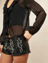 Short de tiro bajo confeccionado en cuero sintético negro, con diseño de costuras decorativas en contraste que forman figuras abstractas tipo western en el frente.