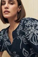 Blusa azul marino con bordados calados en color blanco. Presenta escote en pico, mangas abullonadas con puños elásticos y un diseño de ajuste relajado.