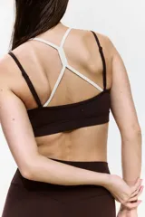Top deportivo en tejido funcional de color marrón con tirantes dobles en color crudo y diseño de superposición. Cuenta con escote redondo y copas con relleno extraíble.