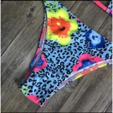 Conjunto de bikini United Uy modelo Mili, con estampado colorido de flores sobre fondo celeste con patrón de leopardo. El corpiño es de diseño triangular con tirantes fucsias y la bombacha es de corte tanga con detalles ajustables en los laterales.