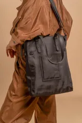 Bolso tipo tote bag de símil cuero color rosa pálido, con asas dobles y detalles de costura en color beige claro. Presenta un bolsillo frontal rectangular aplicado y herrajes metálicos.