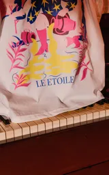 Remera blanca de manga corta y cuello redondo, de calce oversize. Presenta una estampa frontal inspirada en el tarot, con una mujer sentada en un paisaje surrealista, estrellas y la frase "LE ÉTOILE".