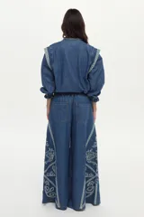 Jean wide leg de denim azul con elástico en la cintura, cordón ajustable y bordados decorativos en los laterales.