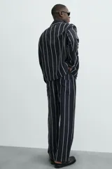 Pantalón de corte relajado, color azul marino, con rayas verticales blancas finas. Presenta cintura elástica ajustable con cordón interior y bolsillos laterales y traseros de plastrón.