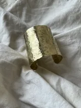 Brazalete ancho de metal plateado con textura martillada.