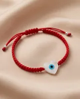 Pulsera de hilo rojo en macramé con dije en forma de corazón de nácar con diseño de ojo turco. Cuenta con cierre regulable con esferas plateadas en las terminaciones.