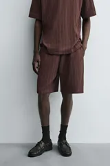 Bermuda de corte relajado color marrón oscuro, confeccionada en tejido jacquard con textura acanalada vertical. Presenta cintura elástica ajustable con cordón, bolsillos delanteros y un bolsillo trasero de plastrón.