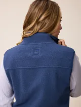 Chaleco de sherpa color beige con cierre frontal completo, cuello alto y bolsillo con cierre en el pecho que incluye un detalle circular con logo.