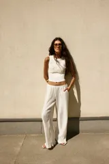 Pantalón blanco roto de tiro alto con cintura elástica y pierna ancha, confeccionado en tejido con textura plisada o arrugada.