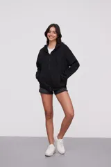 Campera canguro de algodón color negro, con capucha, cierre frontal completo y bolsillos delanteros tipo ojal. Diseño de mangas largas y calce holgado.