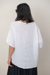 Blusa de lino color marrón oscuro, con escote redondo, mangas cortas amplias y detalle de alforzas verticales en el lateral derecho.