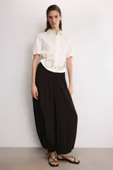 Camisa de manga corta confeccionada en tejido de ramio color blanco. Posee cuello solapa, cierre frontal con botones y detalle de lazos en el acabado de las mangas.