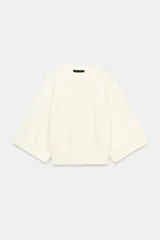 Sweater de punto color blanco marfil, con cuello redondo y mangas cortas de corte ancho. Presenta detalles de rib en el cuello, los puños y el ruedo.