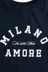 Remera de manga corta color azul marino con cuello redondo y estampado frontal en blanco que dice "MILANO" en arco, "Via della Moda" en letra cursiva pequeña debajo, y "AMORE" centrado abajo.