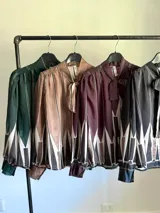 Camisa de manga larga con cuello alto y lazo para atar, confeccionada en tela liviana con estampado geométrico en tonos verde oscuro, blanco, beige y marrón.