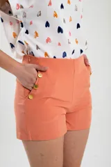 Short de vestir color salmón, de tiro alto, con bolsillos laterales y detalle de botones dorados.