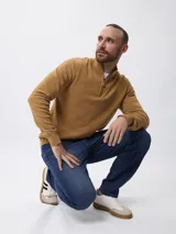 Sweater de tejido de punto color tostado, con cuello alto y cierre frontal parcial. Presenta mangas largas con puños acanalados y un diseño de corte clásico.