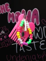Llavero con forma de peine de plástico color rosa brillante, decorado con una pulsera de cuentas de colores vibrantes y dijes colgantes.