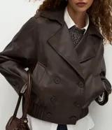 Campera de cuero sintético color marrón oscuro, con diseño de cuello blazer, cierre frontal cruzado, mangas largas estructuradas y ruedo con elástico fruncido.