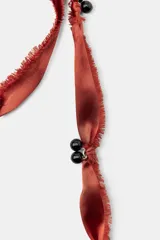 Pack de dos collares de diseño artesanal. El primero presenta una cinta de satén color terracota con flecos, adornada con cuentas negras y un colgante central de madera oscura con una pieza de resina incrustada. El segundo es un collar doble compuesto por una cadena metálica fina y un cordón negro, decorado con cuentas de piedra natural en tonos rojos, marrones y piezas metálicas doradas.
