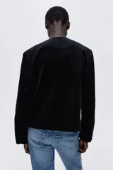 Chaqueta de pana negra con cuello redondo, cierre frontal de botones dorados y dos bolsillos tipo parche en la parte delantera.