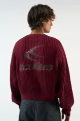 Sweater tejido burdeos de textura acanalada, de corte relajado con cuello redondo, hombros caídos y mangas largas. Cuenta con un gráfico bordado del logo Scuffers en la espalda con estampado de leopardo y terminaciones acanaladas en puños y cintura.