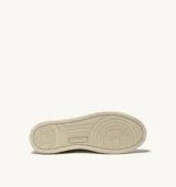 Championes de estilo vintage inspirados en los años 80, confeccionados en cuero blanco con paneles de gamuza gris en la puntera y el talón. Presentan perforaciones en la puntera para mayor ventilación, cordones planos de algodón y un detalle en color verde en el talón. La suela es de goma en tono crema con el logo de la marca.
