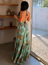 Vestido largo de seda con estampado estilo paisley en tonos verdes, turquesas y naranjas. Presenta un diseño de escote halter con tirantes finos, corte holgado y falda con volados escalonados.