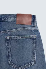 Jeans de corte recto en tono azul clásico con efecto lavado, tiro medio y diseño de cinco bolsillos con cierre frontal de botones.