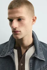 Cazadora cropped fit de denim de algodón, color negro lavado. Presenta cuello solapa, manga larga con puños abotonados, cierre frontal de cremallera y bolsillo superior con cierre de cremallera en el pecho.