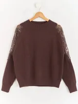 Sweater negro de tejido de punto con cuello redondo y mangas largas. Presenta detalles de transparencias y apliques bordados con pedrería en la parte superior de las mangas.