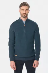 Buzo tejido texturado de color verde oscuro, de corte classic fit, con cuello alto y medio cierre frontal. Presenta detalles de rib en puños y cintura, y una pequeña etiqueta decorativa en el borde inferior.