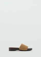 Sandalias de suela de madera color marrón oscuro, con una única tira ancha en piel de serraje color tostado decorada con tachas doradas a lo largo de los bordes.