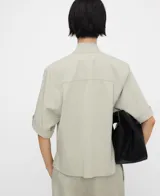 Camisa recta de color verde claro, con cuello tipo tira, manga amplia, botonadura frontal oculta por sopapa y bolsillo en el pecho.