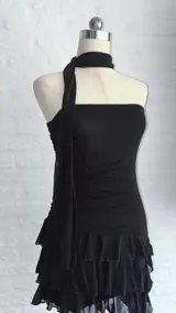 Vestido corto negro de estilo strapless con ajuste drapeado en el torso y falda con volados en capas. Incluye una cinta negra a modo de gargantilla integrada al diseño.