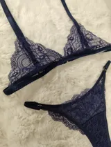 Conjunto de lencería de encaje color azul marino, compuesto por un soutien triangular sin relleno con tirantes regulables y una bombacha colaless ajustable con tiras laterales y detalles de argollas metálicas.
