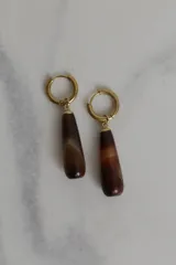 Aros tipo argolla con dije colgante en forma de gota de piedra natural en tonos marrones. Fabricados en acero quirúrgico dorado.
