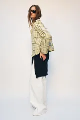 Chaqueta de corte recto confeccionada en tejido con textura de cuadros en tonos amarillos, blancos y negros. Presenta cuello solapa, cierre frontal con botones ocultos, bolsillos de plastrón con solapa en el delantero y mangas largas con puños abotonados.