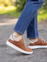Zapatillas urbanas de cuero negro con suela blanca cosida y detalle de textura en el talón.