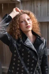 Campera de eco cuero negro con solapas anchas, cierre diagonal metálico y detalle de múltiples ojalillos metálicos distribuidos en el frente y las mangas.