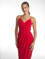 Vestido midi de crepe color rojo, con escote en V cruzado y drapeado en el busto. Presenta una falda envolvente con diseño drapeado que genera una abertura asimétrica en el bajo. Cuenta con tirantes finos y cierre invisible en la espalda.
