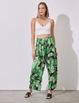 Pantalón largo de seda fría estampada con hojas de palmera en tonos verdes y blancos sobre fondo negro. Tiene pretina ancha elastizada.