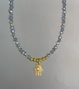 Collar de cristales facetados grises y cuentas doradas, con dije de mano de Fátima (Hamsa) con circonias incrustadas y baño de oro.