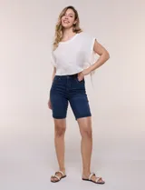 Bermuda de jean azul oscuro con calce ajustado y tecnología push up. Presenta cintura con presillas, cierre frontal con botón metálico, diseño clásico de cinco bolsillos y largo por encima de la rodilla con dobladillo en el ruedo.