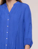 Blusa celeste de silueta suelta y textura liviana, con escote en V, cuello mao y cierre frontal de botones. Cuenta con alforzas verticales en el pecho y mangas tres cuartos con puños elastizados y detalle de galón calado.